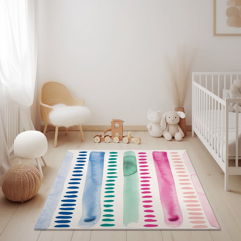 May include: A colorful play rug with watercolor stripes and white polka dots. The rug is in a nursery with a white crib, a wooden toy train, and a wicker chair.
