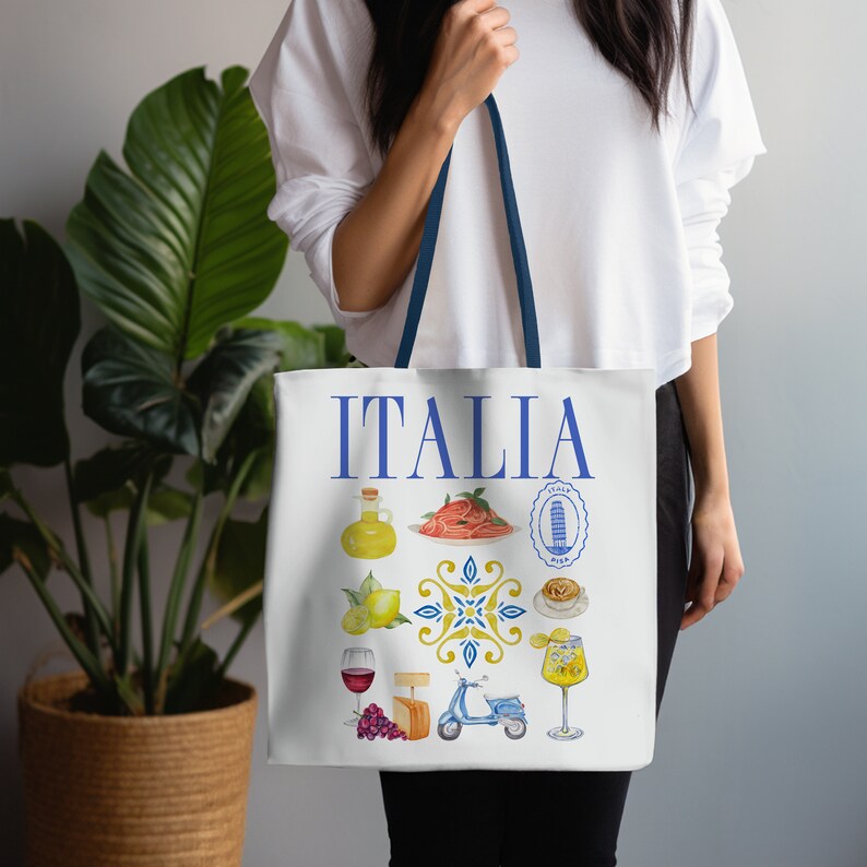 K&ouml;nnte beinhalten: Wei&szlig;e Tragetasche mit marineblauen Tr&auml;gern. Auf der Tasche steht in blauer Schrift das Wort "ITALIA" und Illustrationen italienischer K&uuml;che und Wahrzeichen, wie Pasta, Zitronen und der Schiefe Turm von Pisa.