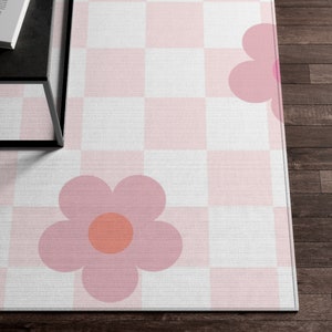 K&ouml;nnte beinhalten: Ein rosa-wei&szlig; karierter Teppich mit zwei rosa Blumen. Die Blumen haben einen Pfirsichkern.