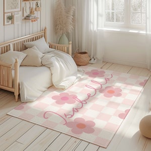 K&ouml;nnte beinhalten: Ein rosa-wei&szlig; karierter Teppich mit einem rosa Blumendesign und dem Namen "Isabella" in Kursivschrift. Der Teppich befindet sich in einem Schlafzimmer mit einem Holzbett und wei&szlig;en Bettw&auml;sche.