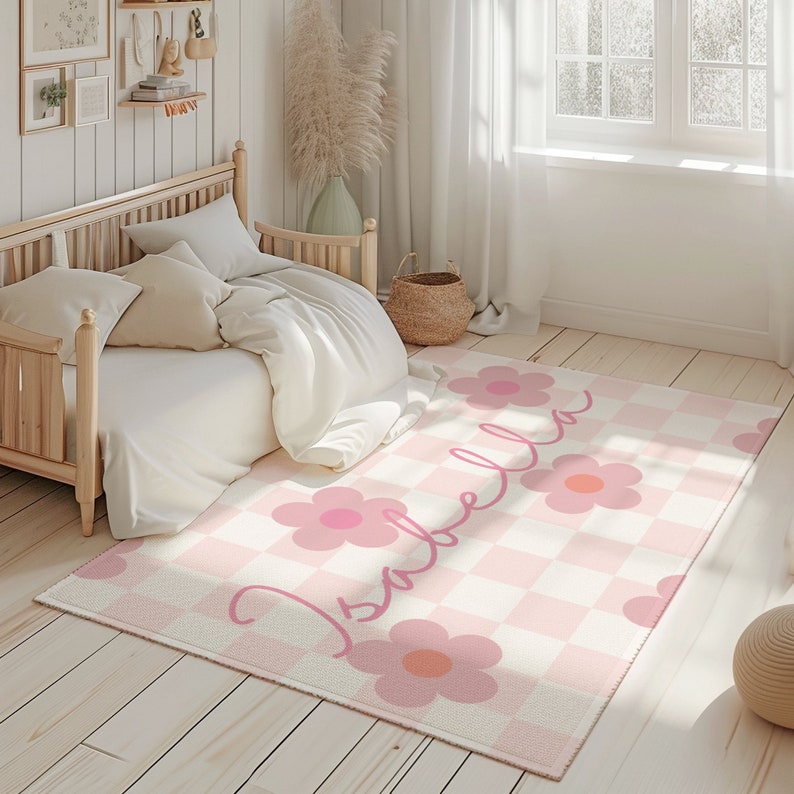 K&ouml;nnte beinhalten: Ein rosa-wei&szlig; karierter Teppich mit einem rosa Blumendesign und dem Namen "Isabella" in Kursivschrift. Der Teppich befindet sich in einem Schlafzimmer mit einem Holzbett und wei&szlig;en Bettw&auml;sche.