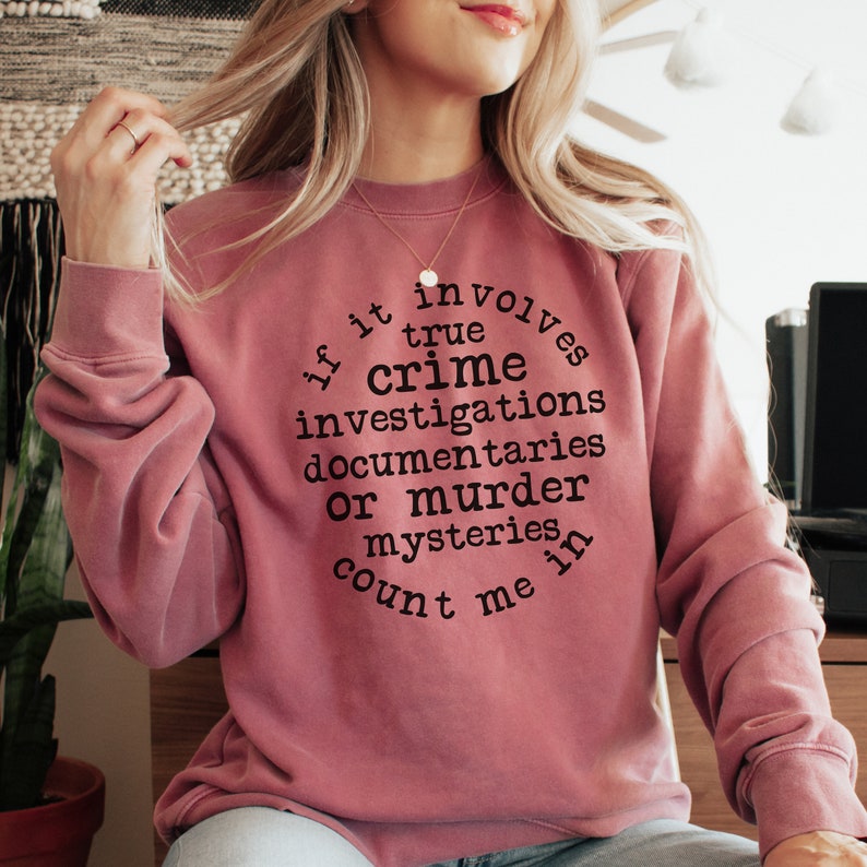 May include: A mauve sweatshirt with a black graphic print that reads "If it involves true crime investigations, documentaries, or murder mysteries, count me in."