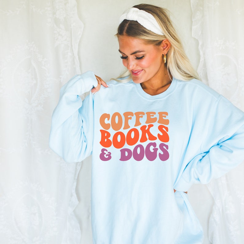 May include: A light blue sweatshirt with the text "COFFEE BOOKS & DOGS" in a retro font with orange, pink, and purple colors.