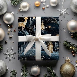 May include: A wrapped gift with a white ribbon and bow, featuring a dark blue and gold winter scene with a deer and houses. The gift is surrounded by silver and gold Christmas ornaments and evergreen sprigs on a gray surface.