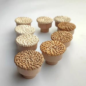 May include: A set of ten round, woven rattan drawer pulls in natural and white colors. The pulls have a wooden base and are perfect for adding a touch of natural texture to any home decor.