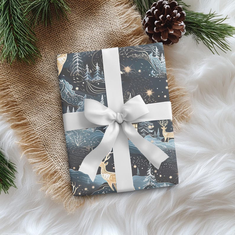 May include: A wrapped gift with a white ribbon and bow. The wrapping paper features a winter landscape design with deer, trees, and stars in shades of blue, gold, and white. The gift is on a white fluffy surface with a burlap accent and pinecone.