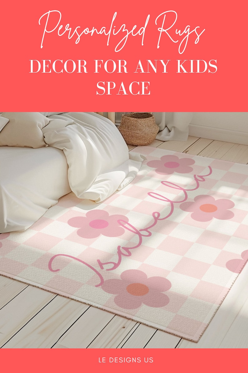 K&ouml;nnte beinhalten: Ein rosa-wei&szlig; karierter Teppich mit einem rosa Blumendesign und dem Namen "Isabella" in Kursivschrift. Der Teppich befindet sich in einem Schlafzimmer mit einem wei&szlig;en Bett und einem Weidenkorb.
