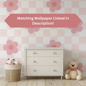 K&ouml;nnte beinhalten: Eine wei&szlig;e Kommode mit drei Schubladen vor einer pinkfarbenen und wei&szlig;en karierten Wand mit pinkfarbenen Blumenaufklebern. Der Text "Matching Wallpaper Linked in Description!" befindet sich auf einem pinkfarbenen Pfeil &uuml;ber der Kommode. Zwei Teddyb&auml;ren stehen auf dem Boden vor der Kommode.