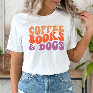 May include: White t-shirt with the text "COFFEE BOOKS & DOGS" in a retro font with orange, pink, and purple colors.