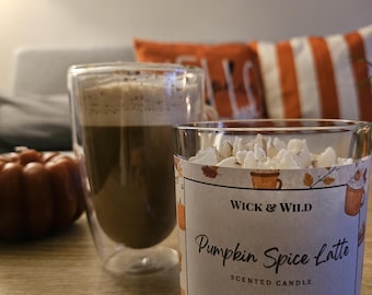 May include: A clear glass candle container with a label reading WICK & WILD Pumpkin Spice Latte SCENTED CANDLE Hand-poured soy candle, featuring a pattern of autumn leaves and mugs, filled with white wax shaped like whipped cream topping.