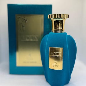 May include: A turquoise perfume bottle with a gold cap and a matching box. The bottle has a textured, velvet-like finish and a gold label with the text "VOUX TURQUOISE" and "Damin". The box has gold lettering.