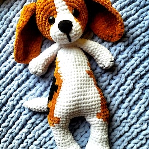Può includere: Un cane di peluche lavorato a uncinetto con pelliccia marrone e bianca. Il cane ha grandi orecchie floppy e un naso nero.