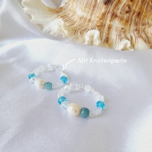Könnte beinhalten: Zwei Perlenarmbänder mit weißen und blauen Perlen. Ein Armband hat eine weiße Perlenperle und das andere hat eine weiße Perlenperle mit dem Text "Mit Knotenperle" auf dem Bild.
