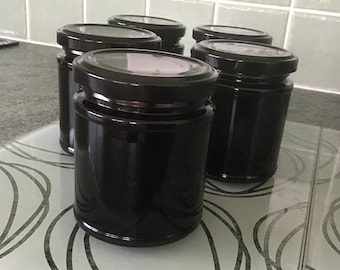 May include: A collection of five cylindrical glass jars with black screw-top lids. Each jar is filled with a dark, opaque substance. The jars are arranged in a group, featuring smooth glass walls and a uniform design for storage or preservation.