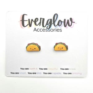 May include: A pair of taco-shaped stud earrings on a white card. The earrings are yellow with green and red details, and each has a smiling face. The card reads "Everglow Accessories" and includes inspirational text.