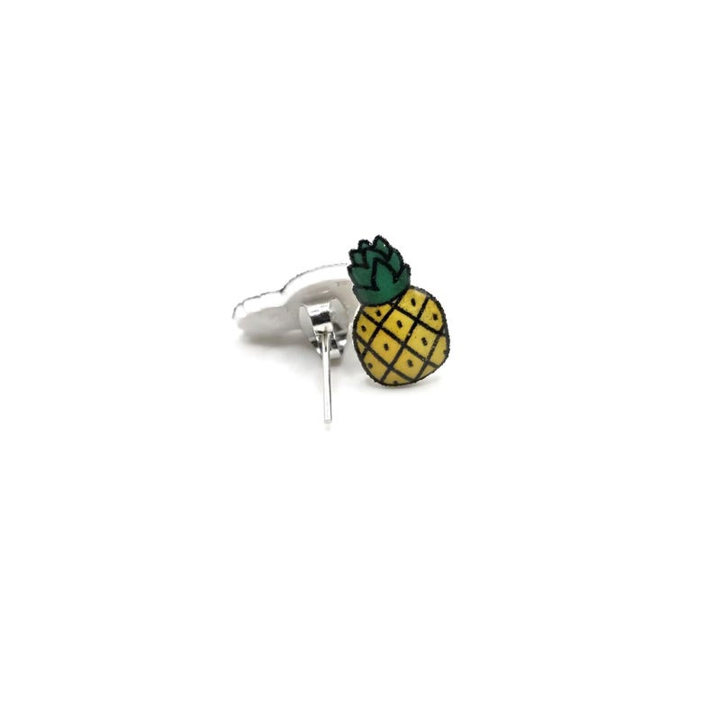 May include: A pair of silver stud earrings with a yellow pineapple design. The pineapple is outlined in black and has a green top.
