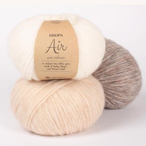 May include: Three balls of DROPS Air uni colour yarn in cream, beige, and taupe. The cream-colored ball has a brown label with the text "DROPS Air uni colour" and "A medium thick blow yarn, made of Baby Alpaca and Merino Wool."