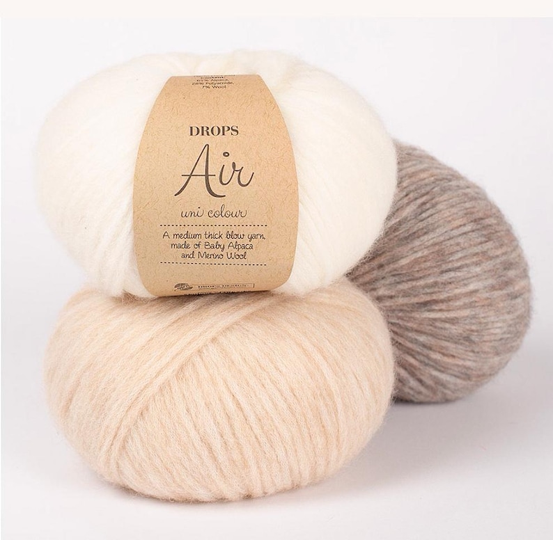 May include: Three balls of DROPS Air uni colour yarn in cream, beige, and taupe. The cream-colored ball has a brown label with the text "DROPS Air uni colour" and "A medium thick blow yarn, made of Baby Alpaca and Merino Wool."