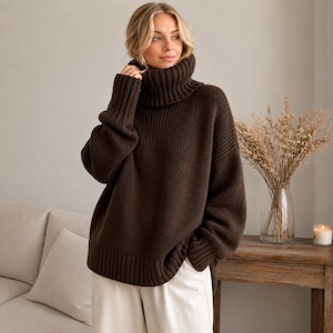 May include: A dark brown, chunky knit sweater featuring a high, ribbed turtleneck collar, long sleeves with ribbed cuffs, and a ribbed hem. The sweater has a relaxed, oversized fit with a thick, textured knit pattern throughout the garment.