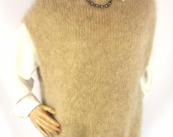 May include: A beige sleeveless knit sweater vest with a fuzzy, brushed texture and a round neckline. The garment is layered over a crisp white collared shirt and features a simple, solid-colored design with a relaxed fit and ribbed hemline.