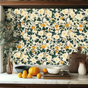 May include: A kitchen with a wallpaper featuring a floral pattern with white flowers and yellow fruit. The wallpaper is on a wall behind a counter with a bowl of oranges, a pumpkin, and a bowl on the counter.