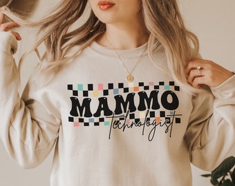 Puede incluir: Una sudadera beige con un patrón de cuadros negros y el texto "MAMMO technologist" en negro y blanco.