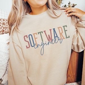 May include: A beige sweatshirt with the text "SOFTWARE engineer" in colorful letters. The letters are in shades of blue, green, pink, and orange.