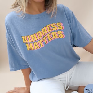 May include: A light blue t-shirt with a yellow and pink graphic that says "Kindness Matters".