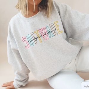 May include: A gray sweatshirt with the text "SOFTWARE engineer" in colorful outlined letters. The sweatshirt is shown on a model wearing white pants.