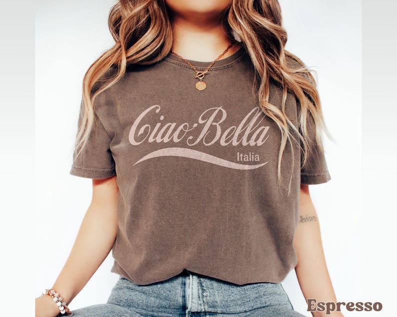 A model wears an espresso shirt that says ciao-bella is a classic script style. It has a wavy ribbon underneath and says Italia.