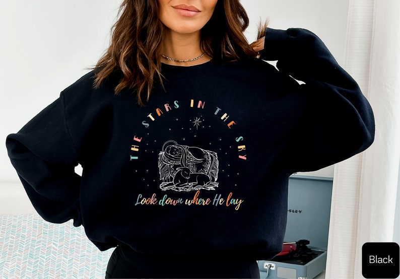 May include: Black sweatshirt with a colorful graphic design featuring a star-shaped circle with the text "The stars in the sky Look down where He lay".