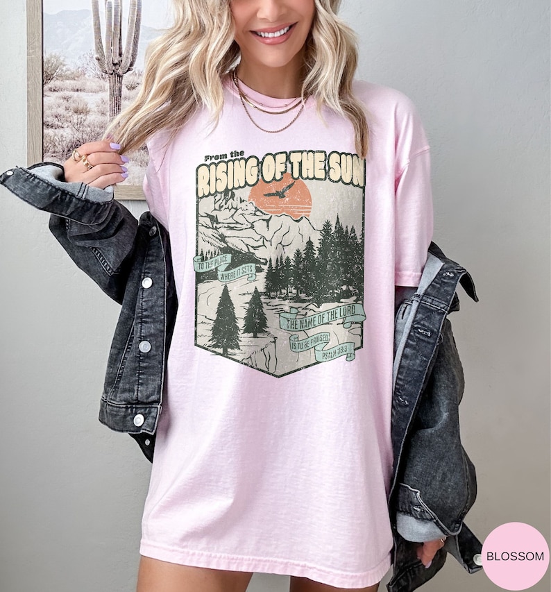 May include: An oversized pink t-shirt with a vintage graphic design featuring a mountain landscape, a bird flying, and the text "From the Rising of the Sun" and "The name of the Lord is to be praised. Psalm 113:3".