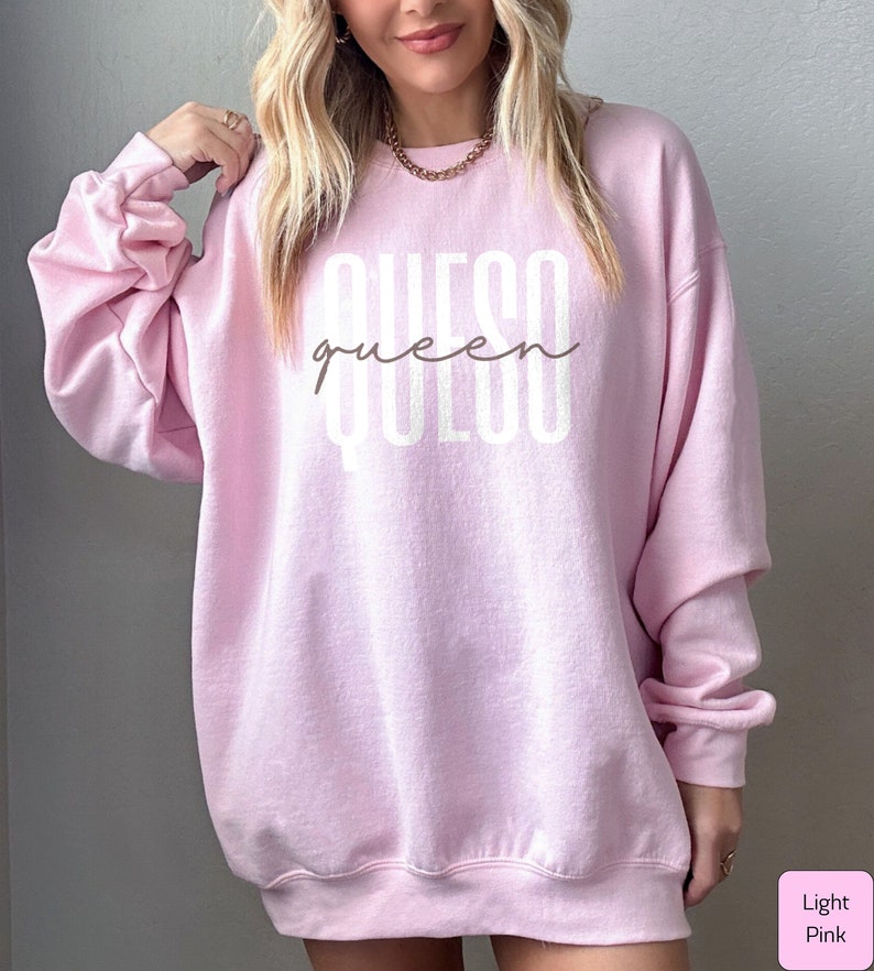 May include: Light pink sweatshirt with the text "queso queen" in white lettering.