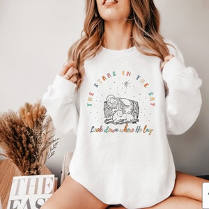 May include: White sweatshirt with a colorful graphic design featuring a manger scene with the text "The stars in the sky Look down where He lay".