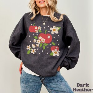 May include: A dark heather grey sweatshirt with a vintage-style graphic of red apples and white flowers.