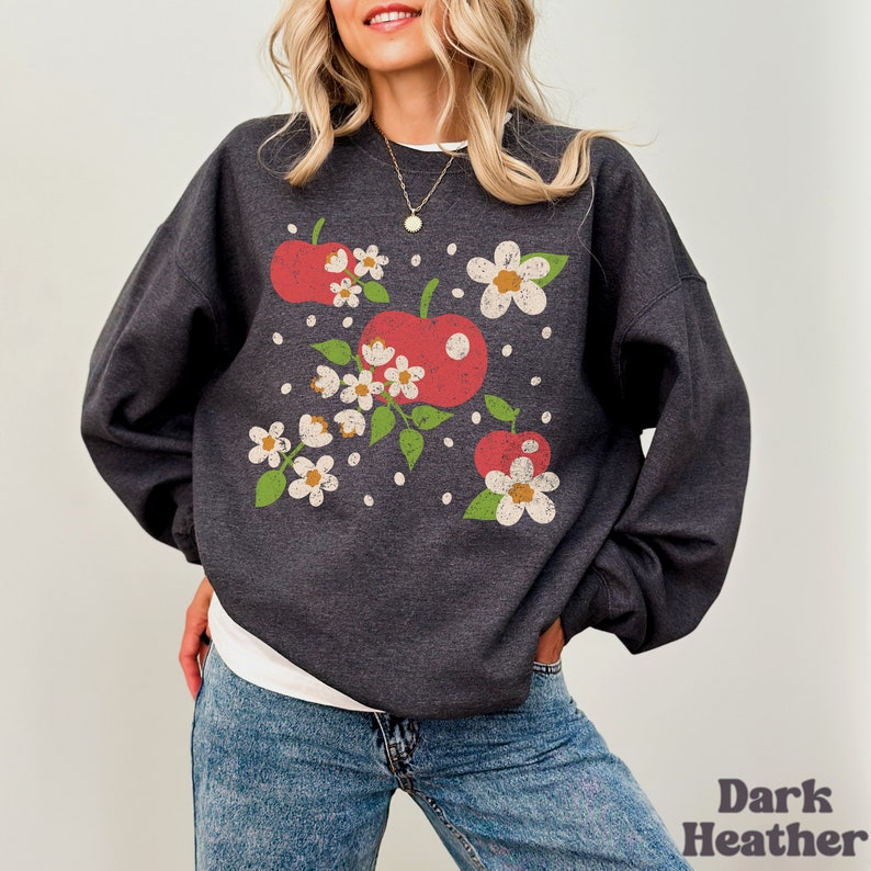 May include: A dark heather grey sweatshirt with a vintage-style graphic of red apples and white flowers.
