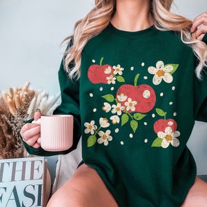 May include: A forest green sweatshirt with a vintage-style graphic print of red apples and white flowers.
