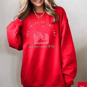 May include: Red sweatshirt with a Christmas-themed design featuring a nativity scene and the text "The stars in the sky look down where He lay."