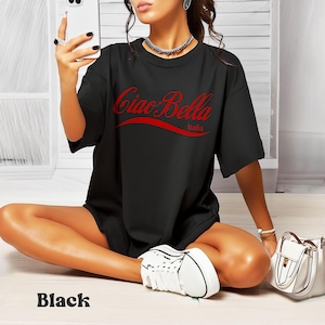 A model wears a black shirt that says ciao-bella is a classic script style. It has a wavy ribbon underneath and says Italia.