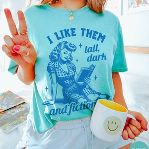 A model wears a chalky mint shirt that has a retro design all in medium blue that days I like them tall, dark and fictional, with a woman from the 1950s sittings and reading a book.