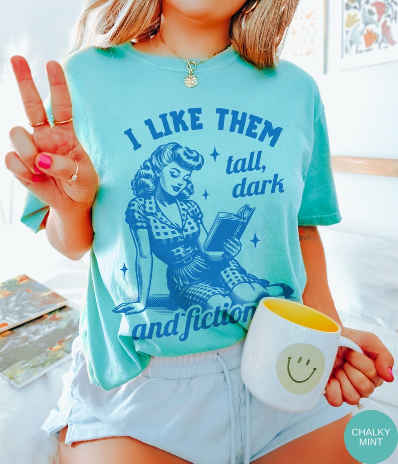A model wears a chalky mint shirt that has a retro design all in medium blue that days I like them tall, dark and fictional, with a woman from the 1950s sittings and reading a book.