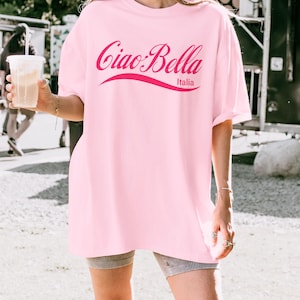A model wears a blossom shirt that says ciao-bella is a classic script style. It has a wavy ribbon underneath and says Italia.
