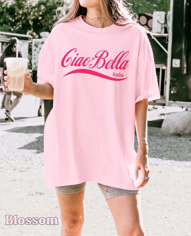 A model wears a blossom shirt that says ciao-bella is a classic script style. It has a wavy ribbon underneath and says Italia.
