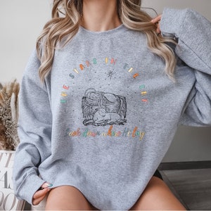 May include: A gray sweatshirt with a colorful graphic design that says "The stars in the sky look down where he lay". The graphic features a star, a manger, and a baby.