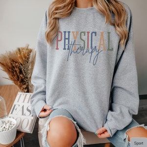 May include: A gray sweatshirt with the text "PHYSICAL therapy" in colorful letters. The sweatshirt is being worn by a person with long blonde hair.