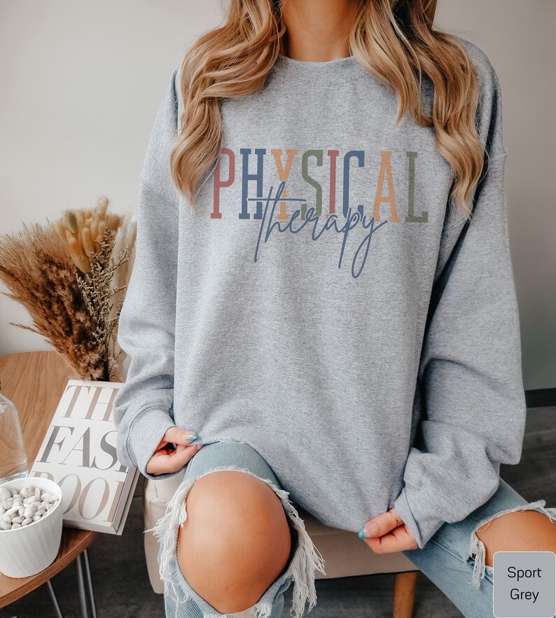 May include: A gray sweatshirt with the text "PHYSICAL therapy" in colorful letters. The sweatshirt is being worn by a person with long blonde hair.