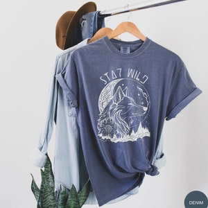 May include: A dark blue t-shirt with a white wolf howling at the moon graphic and the text "STAY WILD".