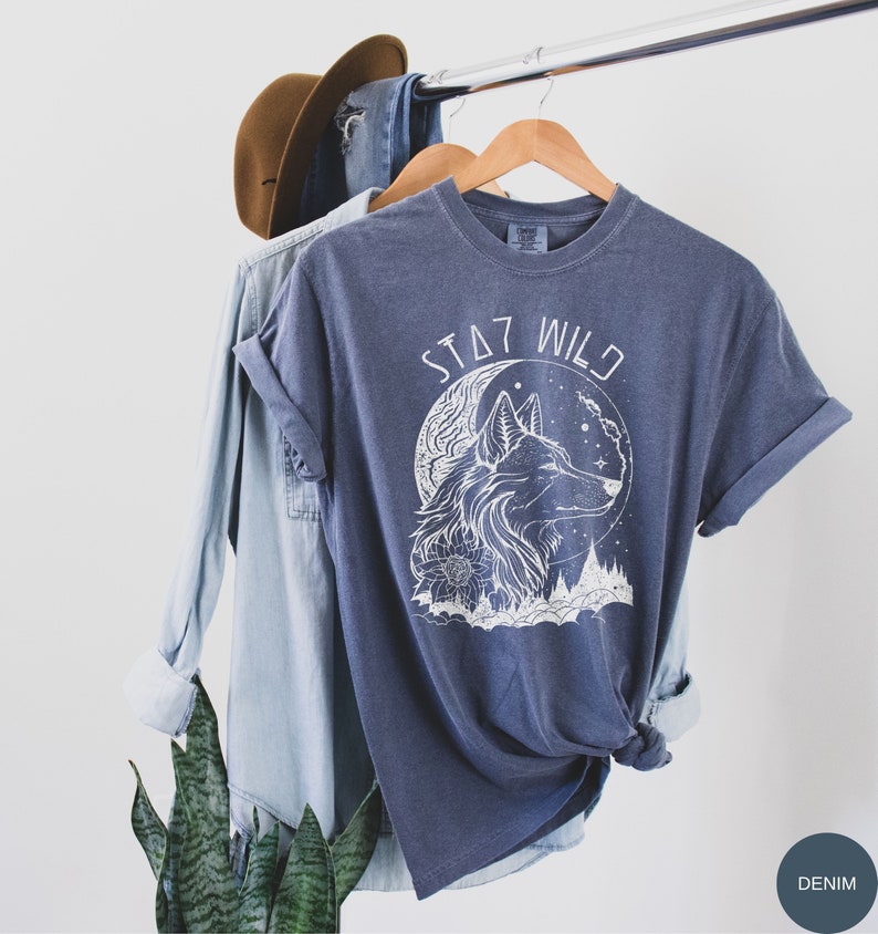 May include: A dark blue t-shirt with a white wolf howling at the moon graphic and the text "STAY WILD".