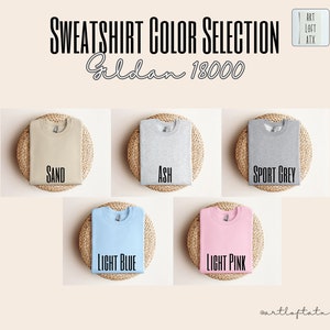 May include: Five folded Gildan 18000 sweatshirts in different colors: sand, ash, sport grey, light blue, and light pink. Each sweatshirt is displayed on a woven straw mat.