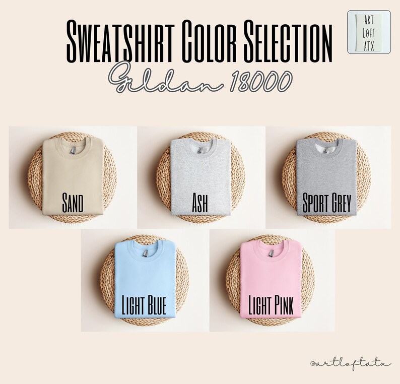 May include: Five folded Gildan 18000 sweatshirts in different colors: sand, ash, sport grey, light blue, and light pink. Each sweatshirt is displayed on a woven straw mat.